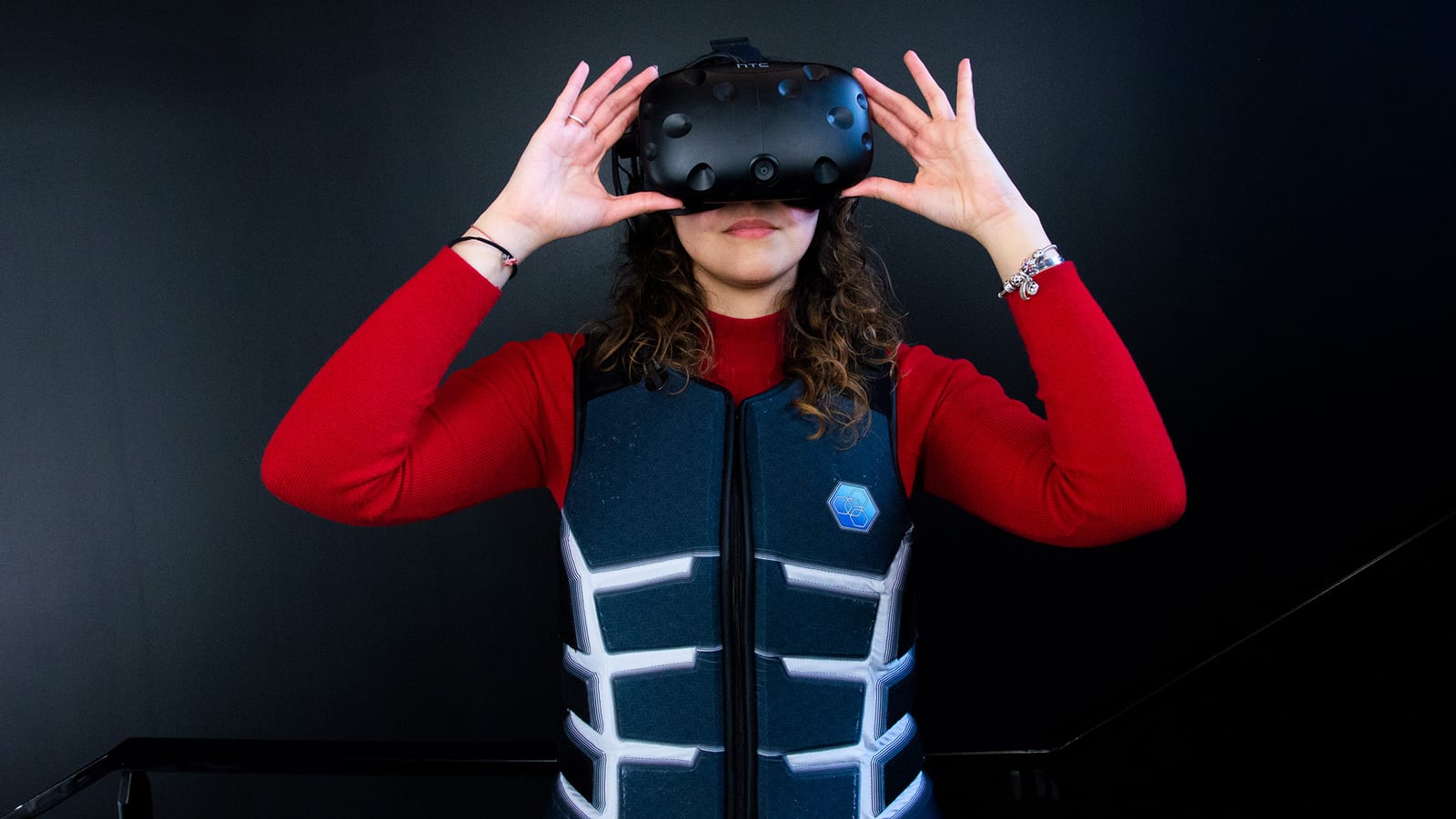 Une joueuse ajuste un casque HTC Vive, la veste Skinetic portée sur un pull rouge.